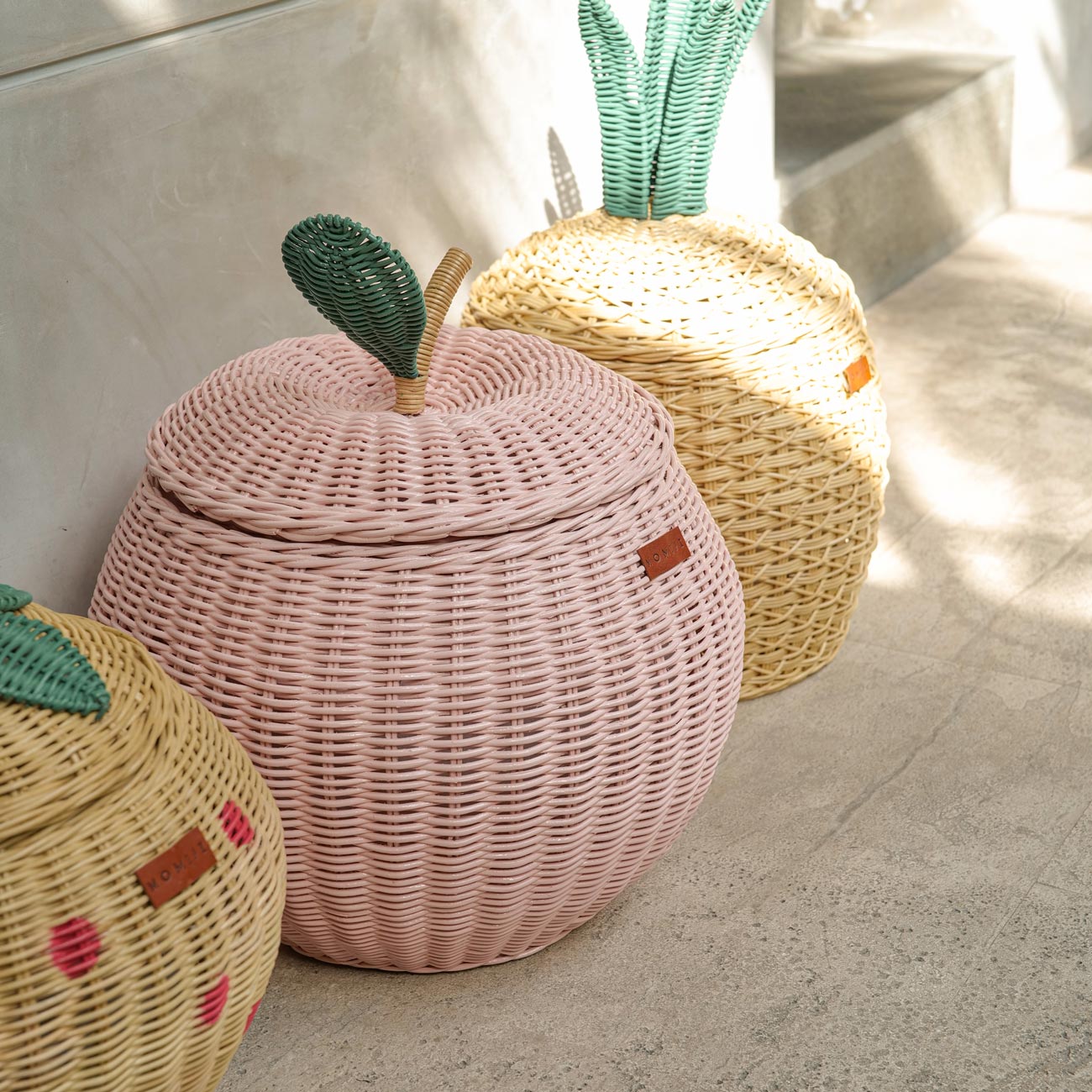 Pink Apple Rattan Storage Basket next to Natural Pineapple Rattan Storage basket and Strawberry Rattan Storage Basket in medium sizes by MOMIJI.