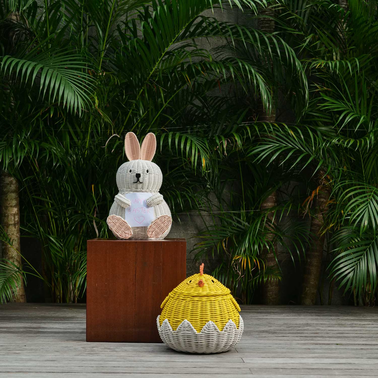 Decorative Bunny Rattan Storage Basket and Chick Rattan Storage Basket by MOMIJI on a wooden platform against a green leafy background.