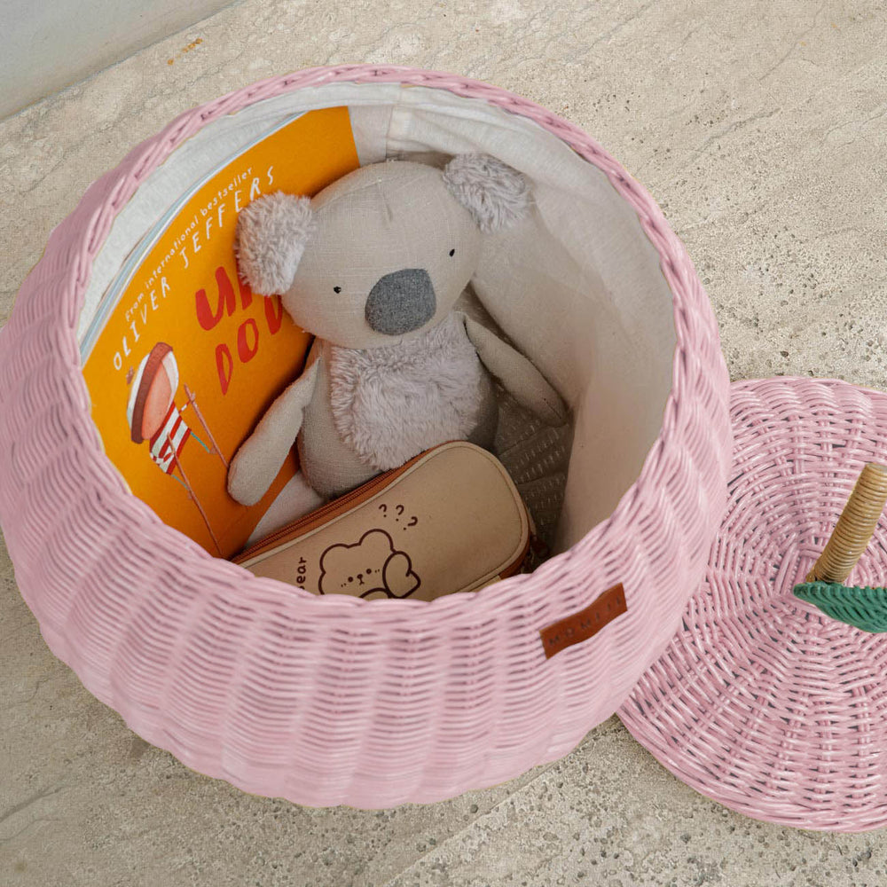 Pink apple rattan storage basket by MOMIJI with toys and books inside.