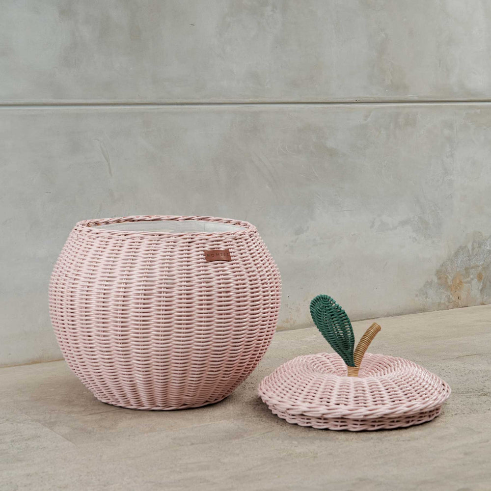 Pink apple rattan storage basket by MOMIJI with lid on the floor.