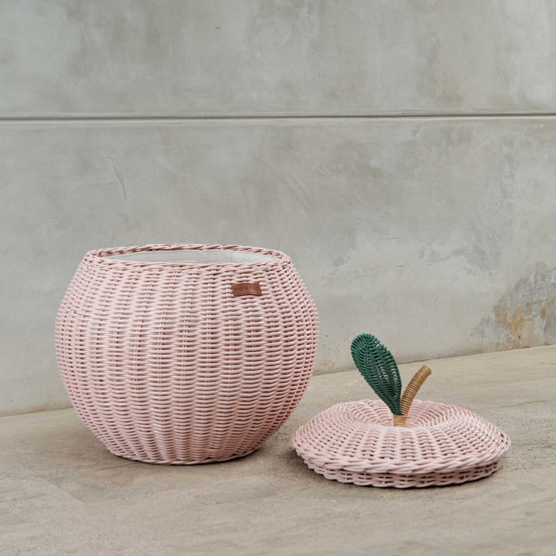 Pink apple rattan storage basket by MOMIJI with lid on the floor.