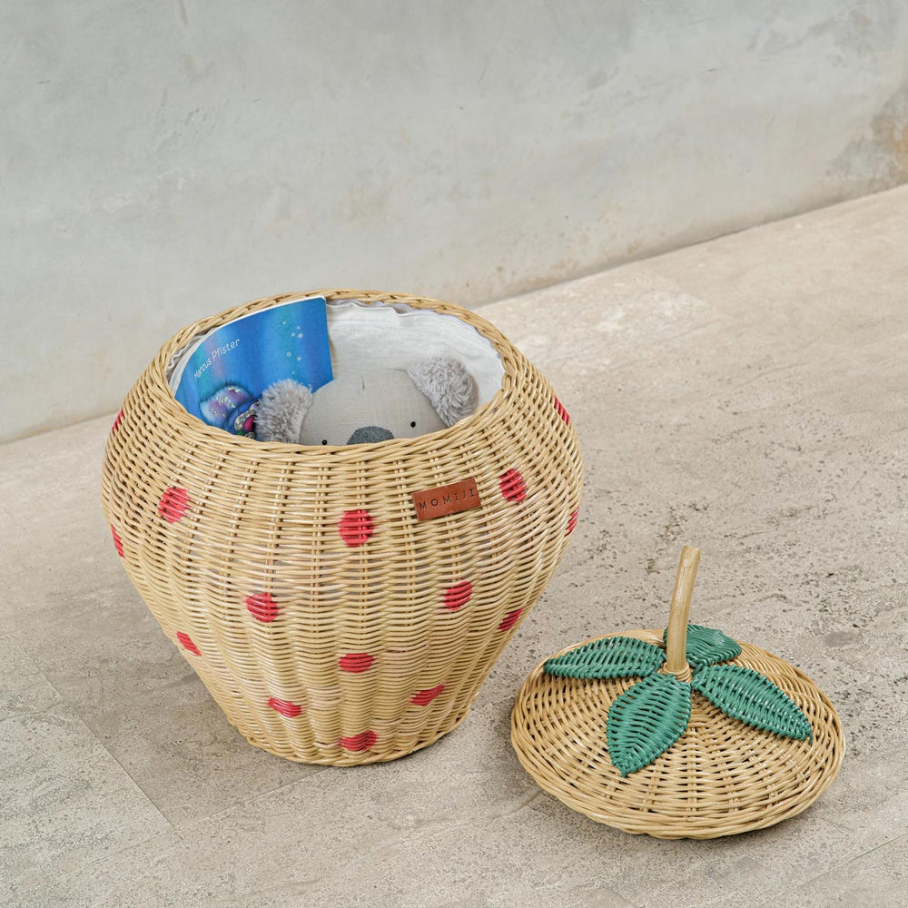 Opened Strawberry Rattan Storage Basket with a book, stuffed toy and a pouch inside, lid on the floor.