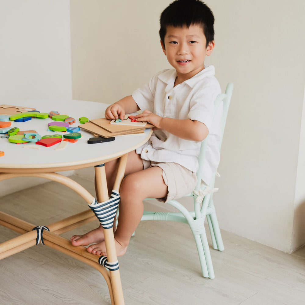 Child sitting on a mint green Bunny rattan chair by MOMIJI while playing with educational toys in a bright and playful room.