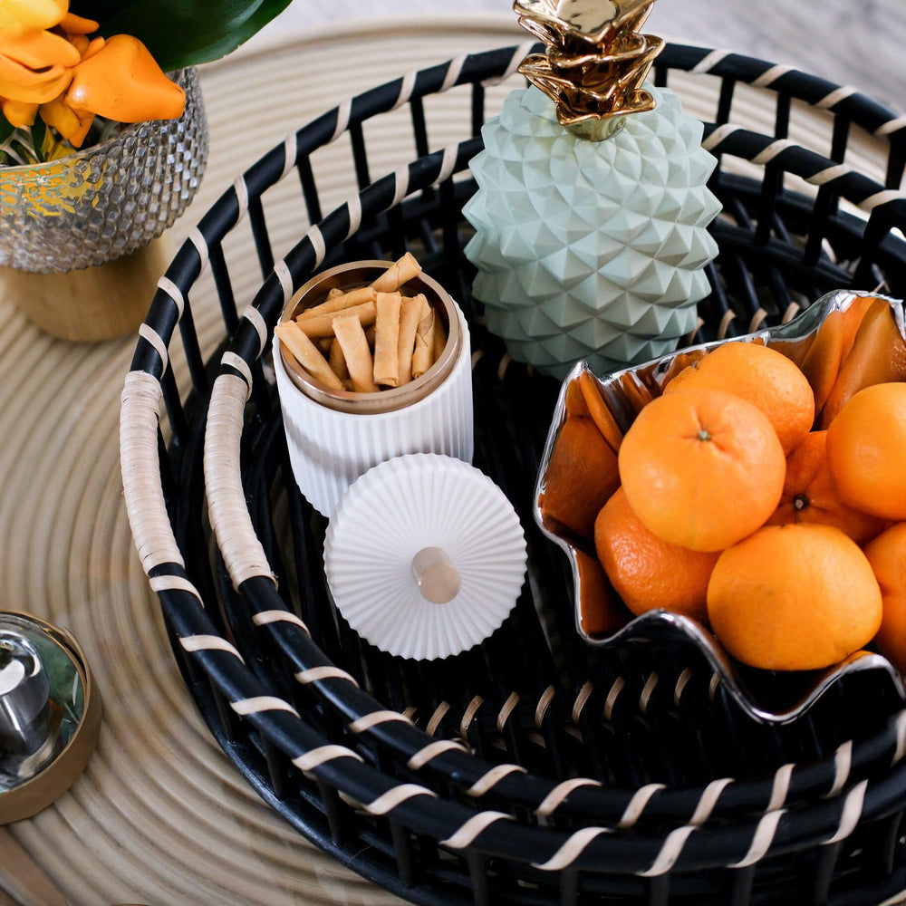 Handcrafted Maru Tray Set by MOMIJI in balck and natural stripe rattan with oranges, cookies, and a decorative pineapple on the table.