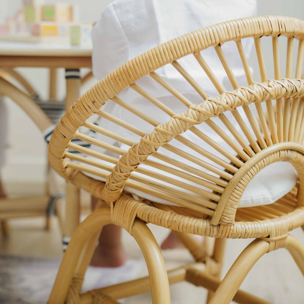 Back view of a child sitting on the natural handcrafted rattan Maya Kids Chair by MOMIJI in an indoor room, showing smooth and supportive rattan weaving designed for child-safe comfort.