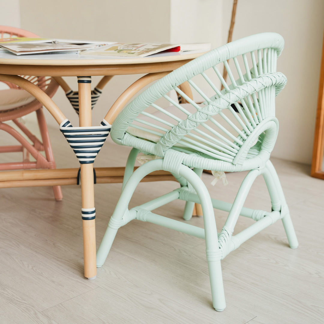 Back view of the handcrafted Mint Green rattan Maya Kids Chair by MOMIJI, showcasing its smooth and supportive rattan weaving designed for child-safe comfort, paired with an Aulia Kids Table styled with children's books.