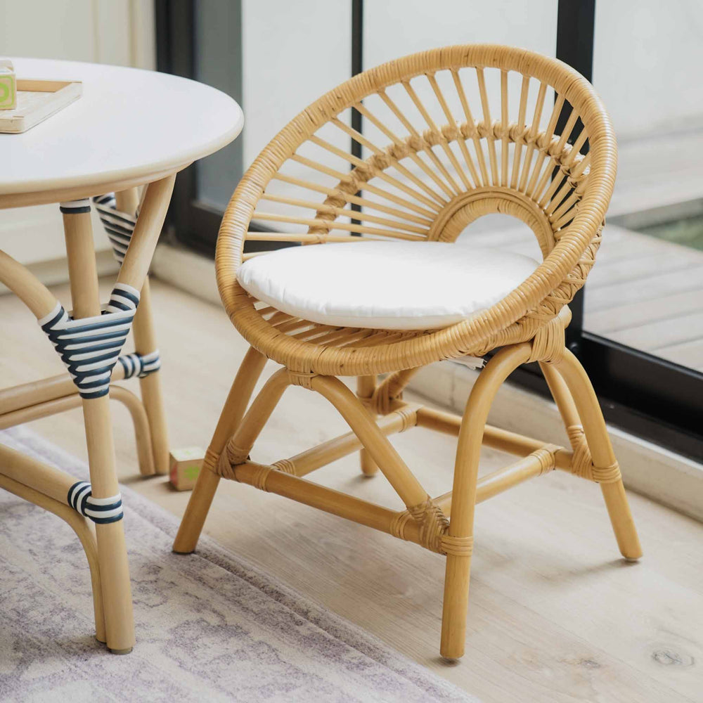 Angled view of the handcrafted natural rattan Maya Kids Chair by MOMIJI with a comfortable removable white cushion, paired with a matching Aulia Kids Table topped with colourful building blocks in a playful children's room.