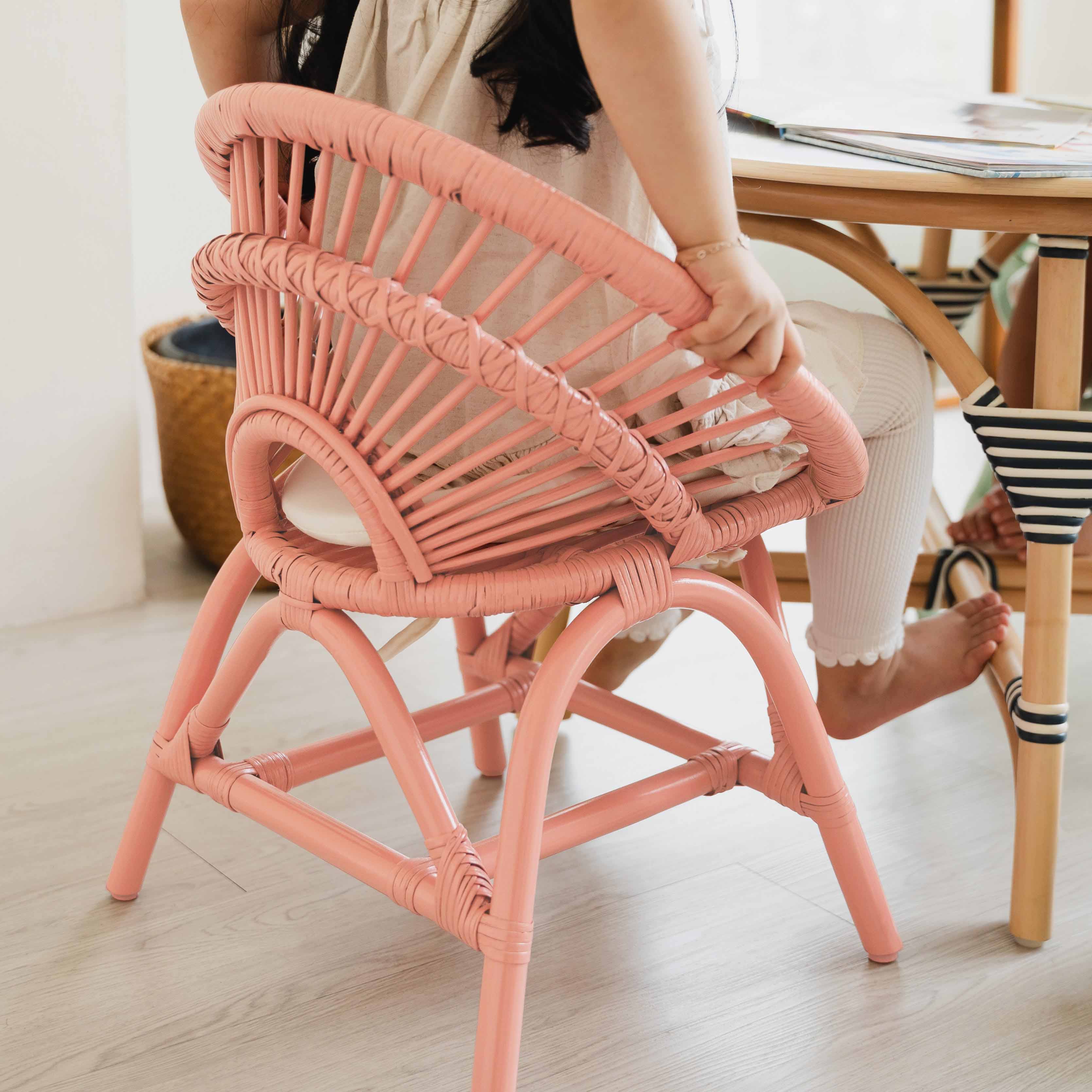 Back view of a child sitting on the handcrafted natural rattan Maya Kids Chair by MOMIJI at an Aulia Kids Table, showcasing the chair's smooth and supportive rattan weaving and the table's rounded edging designed for child-safe comfort while playing with colourful building blocks.