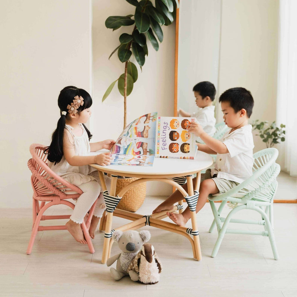 Two children sitting on Maya Kids Chairs peach pink and mint green by MOMIJI reading books in a room with a mirror and plants.