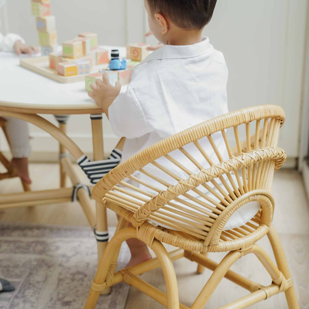 Back view of a child sitting on the handcrafted natural rattan Maya Kids Chair by MOMIJI while playing with colourful building blocks, showcasing the smooth and supportive rattan weaving designed for child-safe comfort.