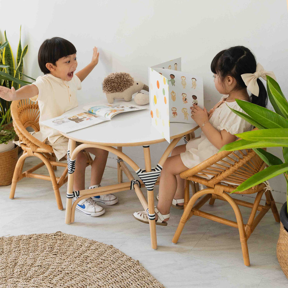Child sitting on the Maya Kids Chair by MOMIJI while playing and reading books at a table in a room with plants.