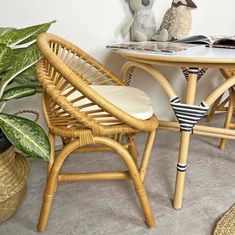 Side view of the Maya Kids Chair by MOMIJI with a table, books, and toys in a room with plants.