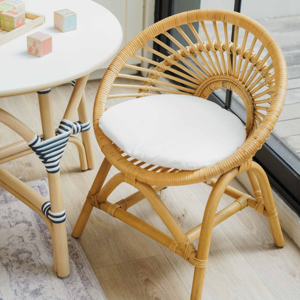 Top view of the handcrafted natural rattan Maya Kids Chair by MOMIJI, showcasing its supportive child-friendly backrest and comfortable removable white seat cushion, styled with a matching rattan table in a playful room