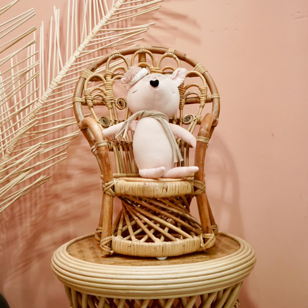 Doll seated on the handcrafted rattan wicker Mini Peacock Doll Chair by MOMIJI placed on a rattan table with decorative elements.