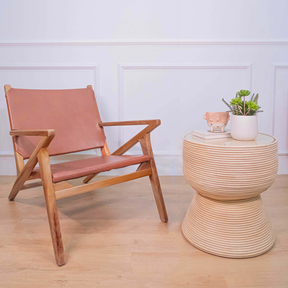 A brown Monty Leather Lounge Chair by MOMIJI with wooden frame and armrests, placed in a room with a round side table and decorative items.