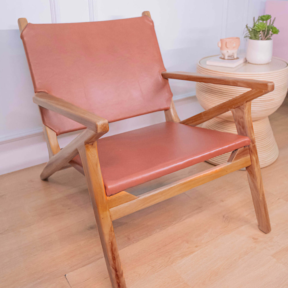 Side view of the brown Monty Leather Lounge Chair by MOMIJI beside a round side table.