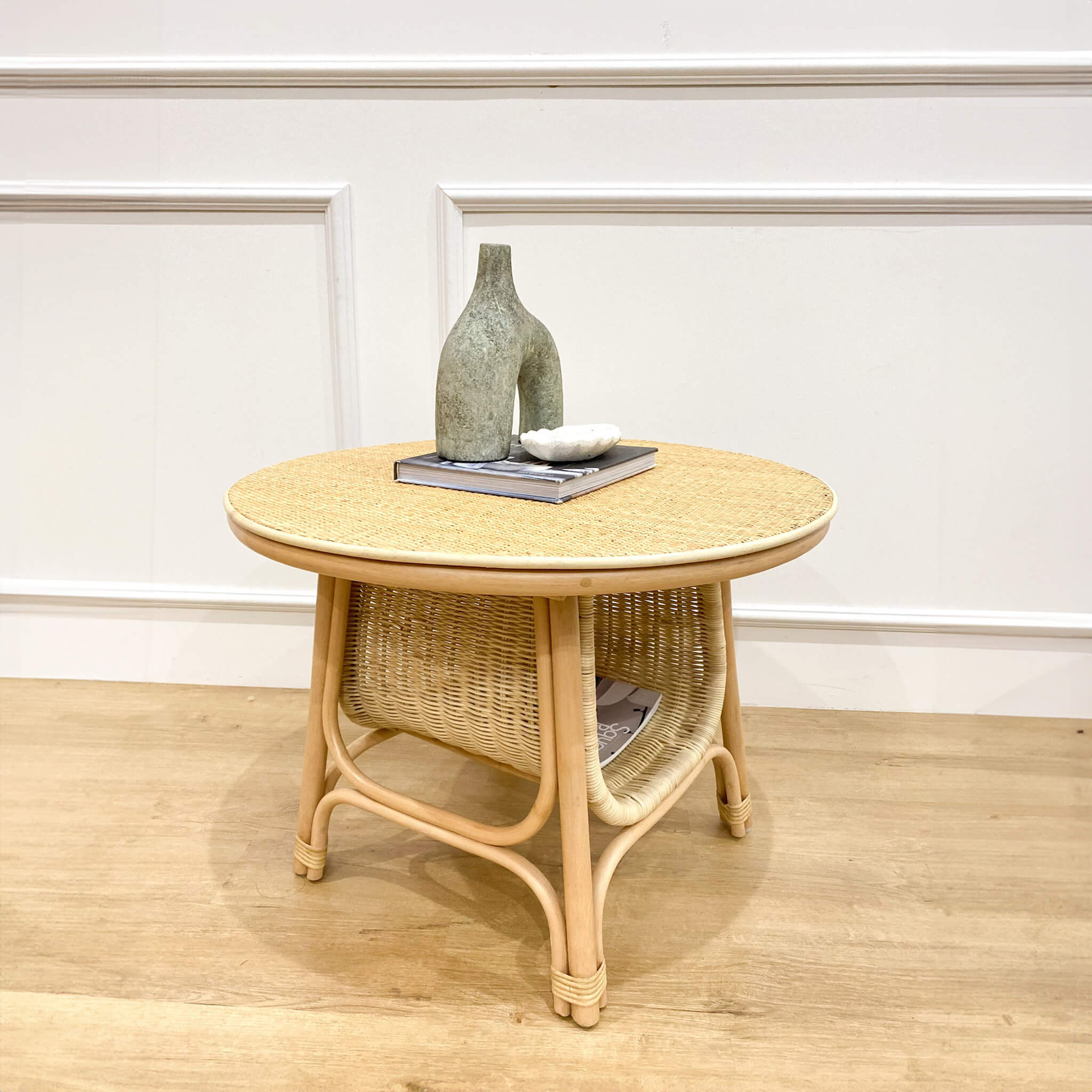 Naia Coffee Table by MOMIJI styled with books and a decorative vase on top, with additional books stored on the handwoven rattan lower shelf.