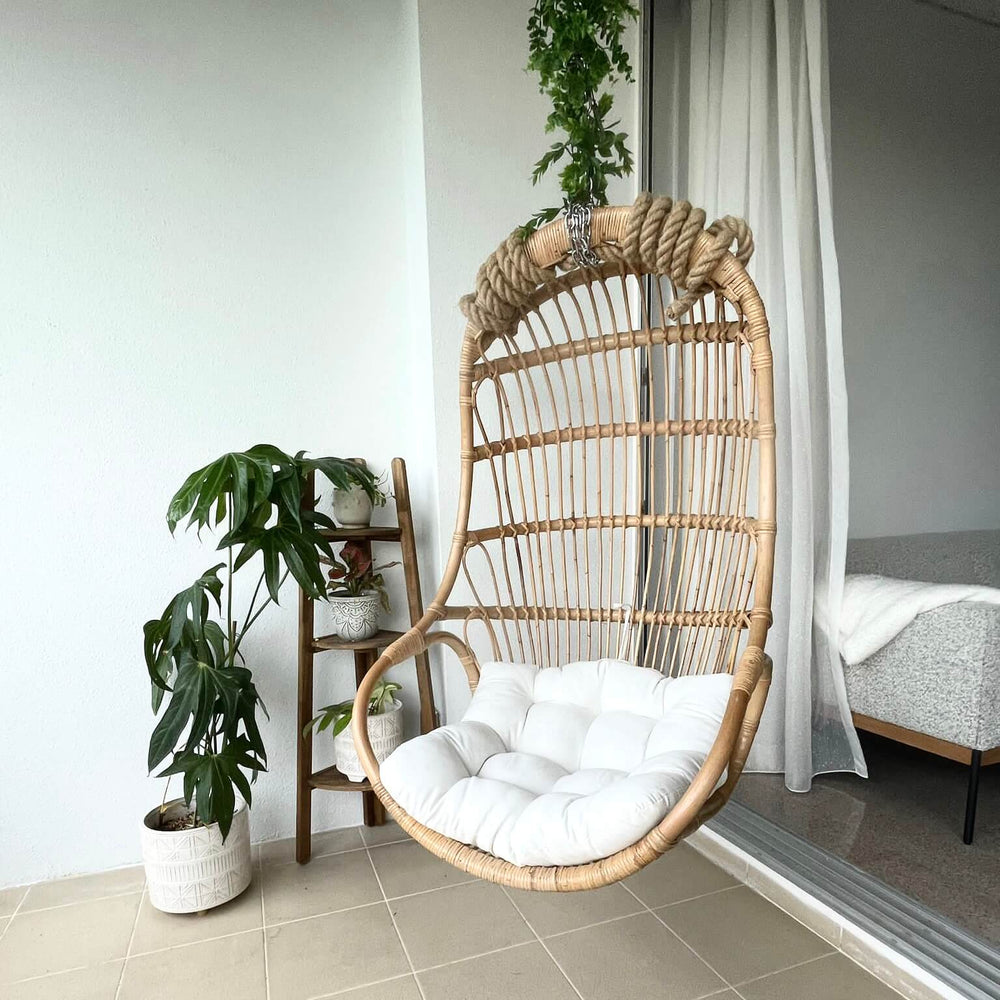 Nest Hanging Chair by MOMIJI with a white cushion, styled outdoors with greenery behind.