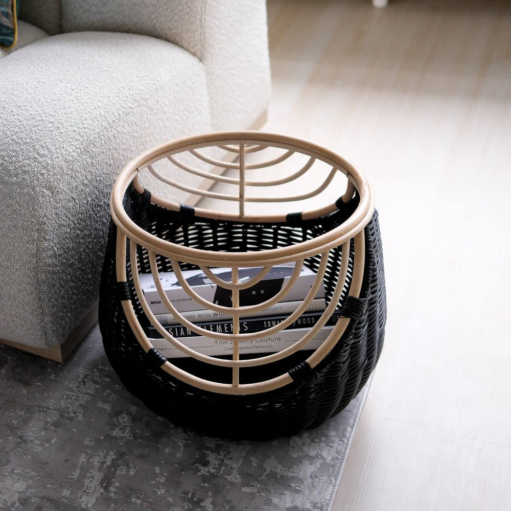 Top view of handcrafted rattan wicker Nikko Basket by MOMIJI featuring black weaving with natural rattan accents, filled with books on a rug in a room with a sofa.