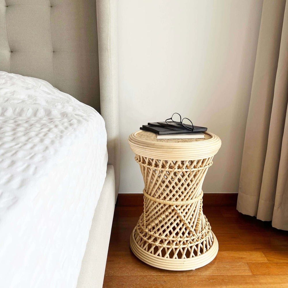 Handcrafted Palawan rattan Stool by MOMIJI styled as a side table next to a bed with white bedding, topped with books and eyeglasses.