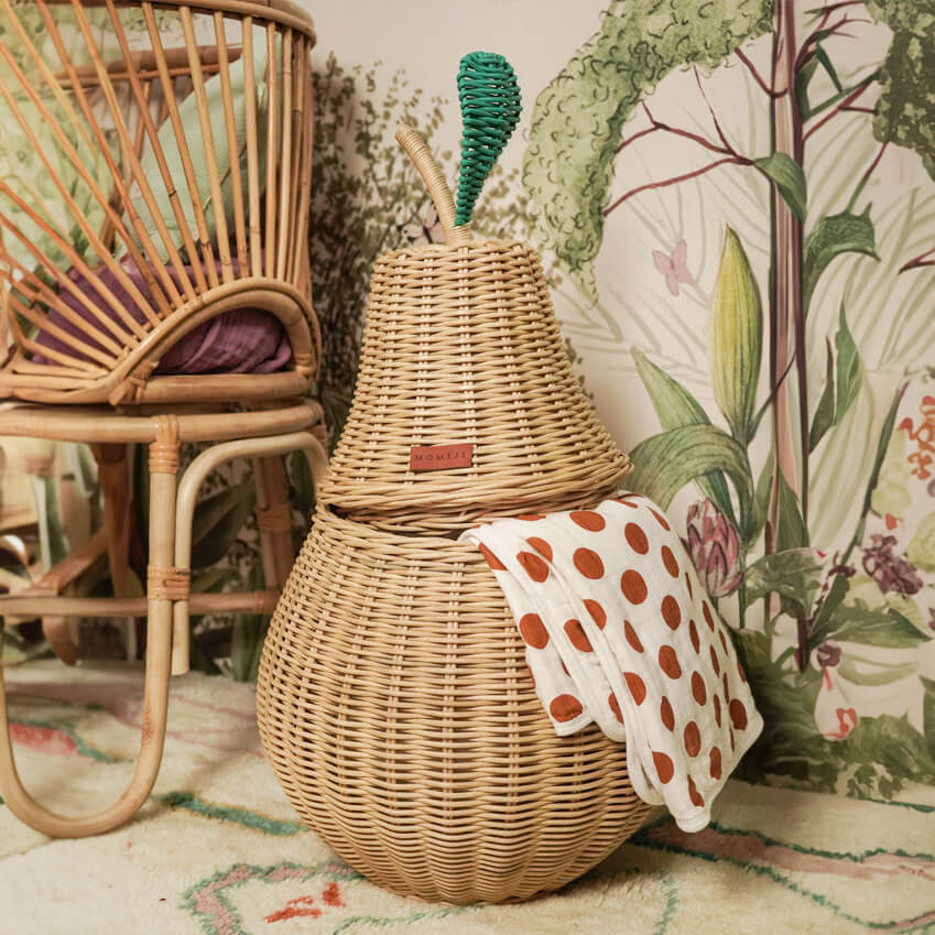 Natural handcrafted Pear Rattan Storage Basket by MOMIJI styled on  a rug with a polka dot towel against a floral wall, serving as playful storage.