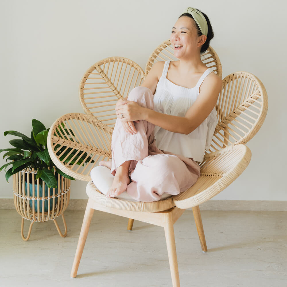 Woman smiling while sitting on Petal Chair by MOMIJI in a cozy living room with plants.