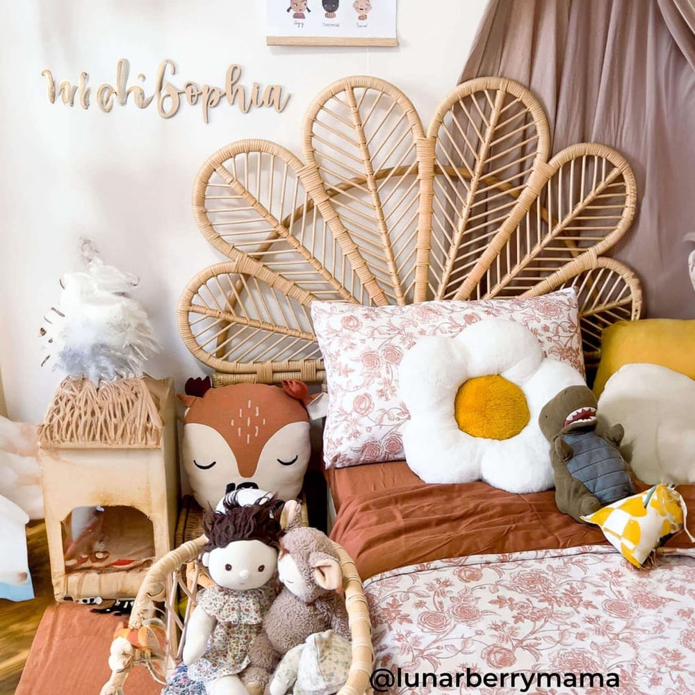Petal Headboard by MOMIJI installed on a child’s bed with dolls, featuring a petal-shaped handwoven rattan headboard.