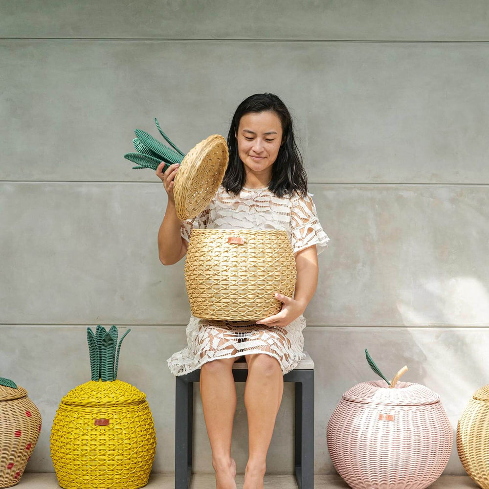 Woman Opening Pineapple Rattan Storage Basket by MOMIJI with fruit rattan basket collection on the floor.