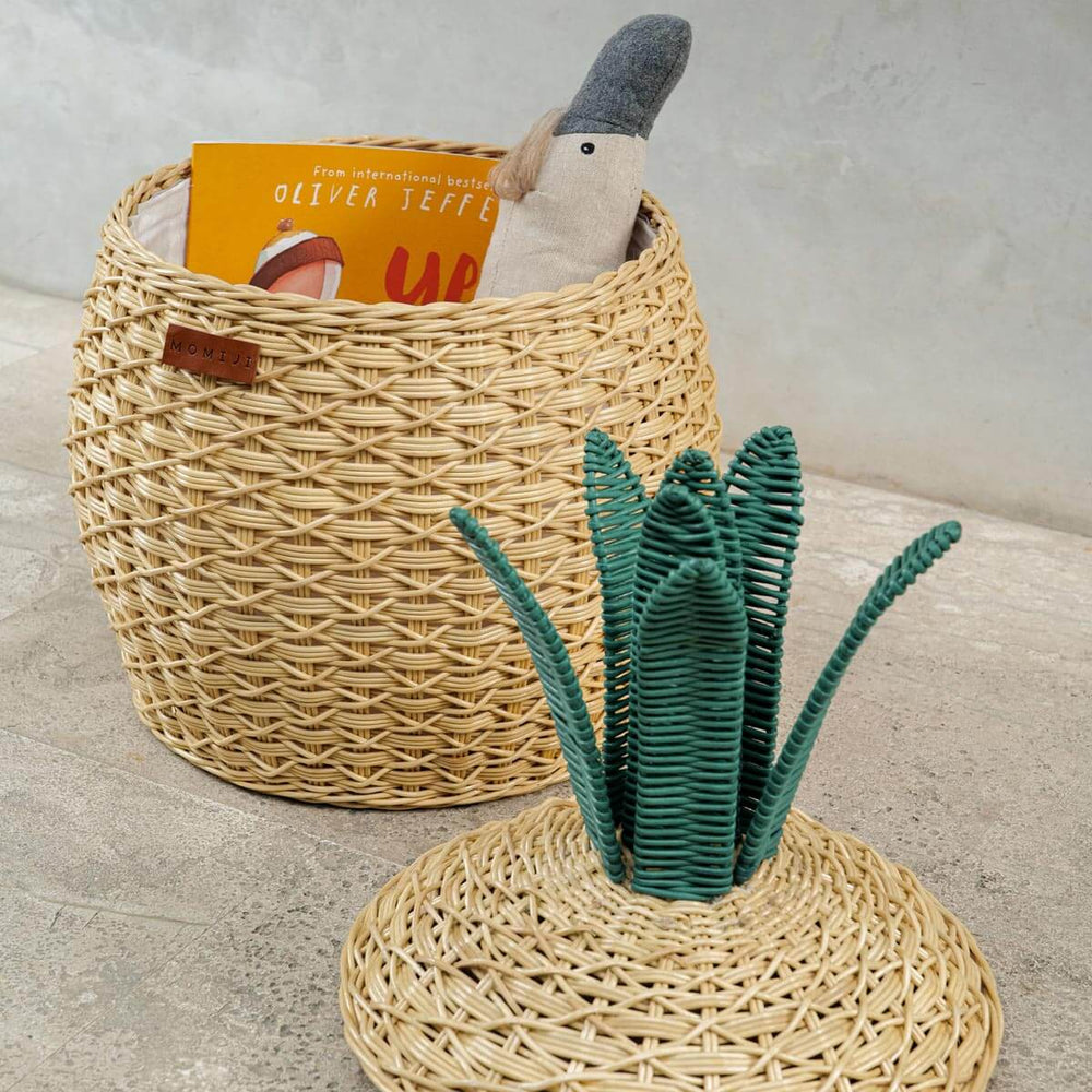 Side view of Pineapple Rattan Storage Basket, opened lid on the floor with toys and books Inside.