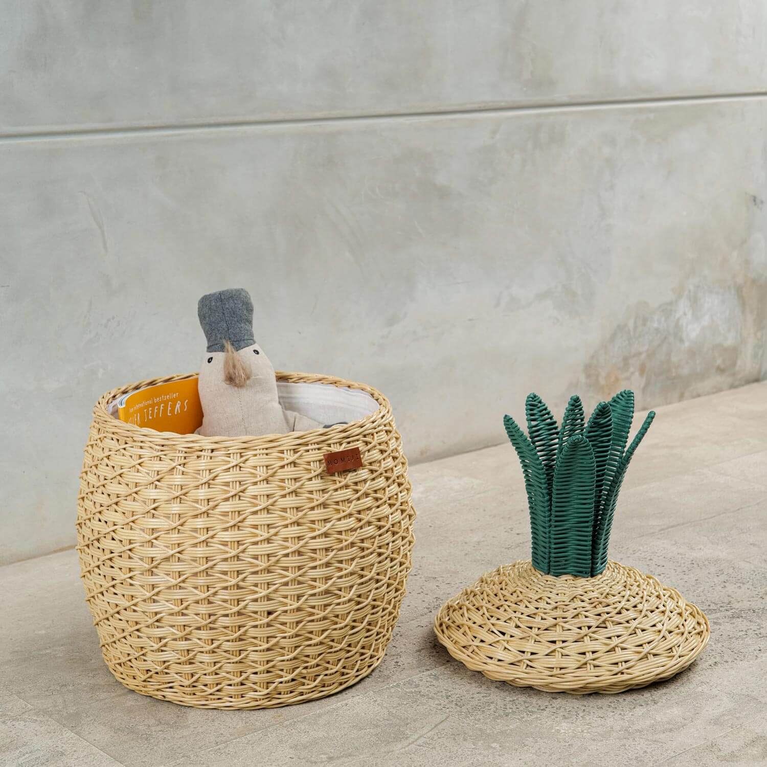 Pineapple Rattan Storage Basket, opened lid on the floor with toys and books Inside.