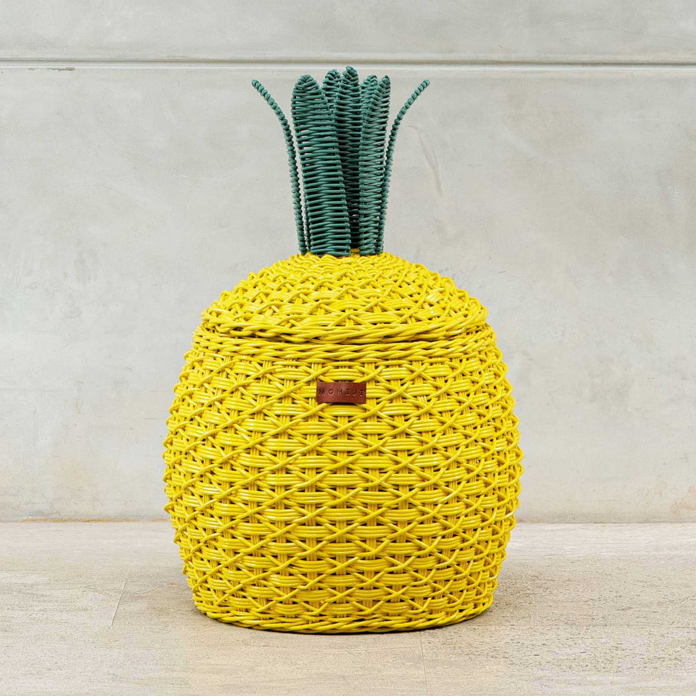 Front view of yellow Pineapple Rattan Storage Basket on a light concrete floor.