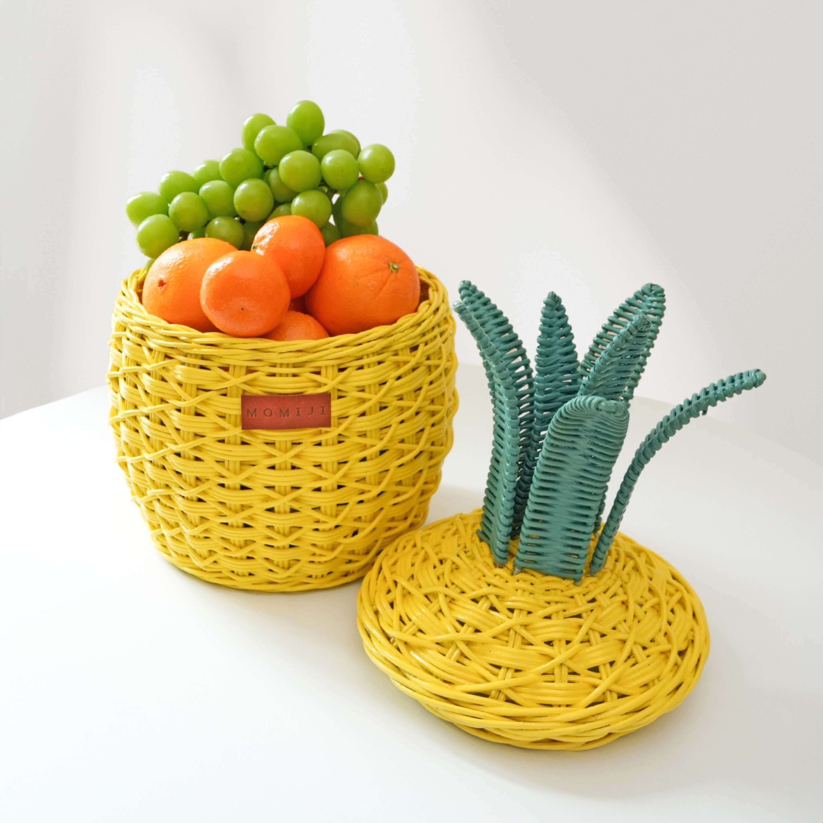 Handcrafted yellow pineapple rattan storage basket in small size by MOMIJI shown with the lid off and filled with fruits, highlighting its use as a decorative storage basket.