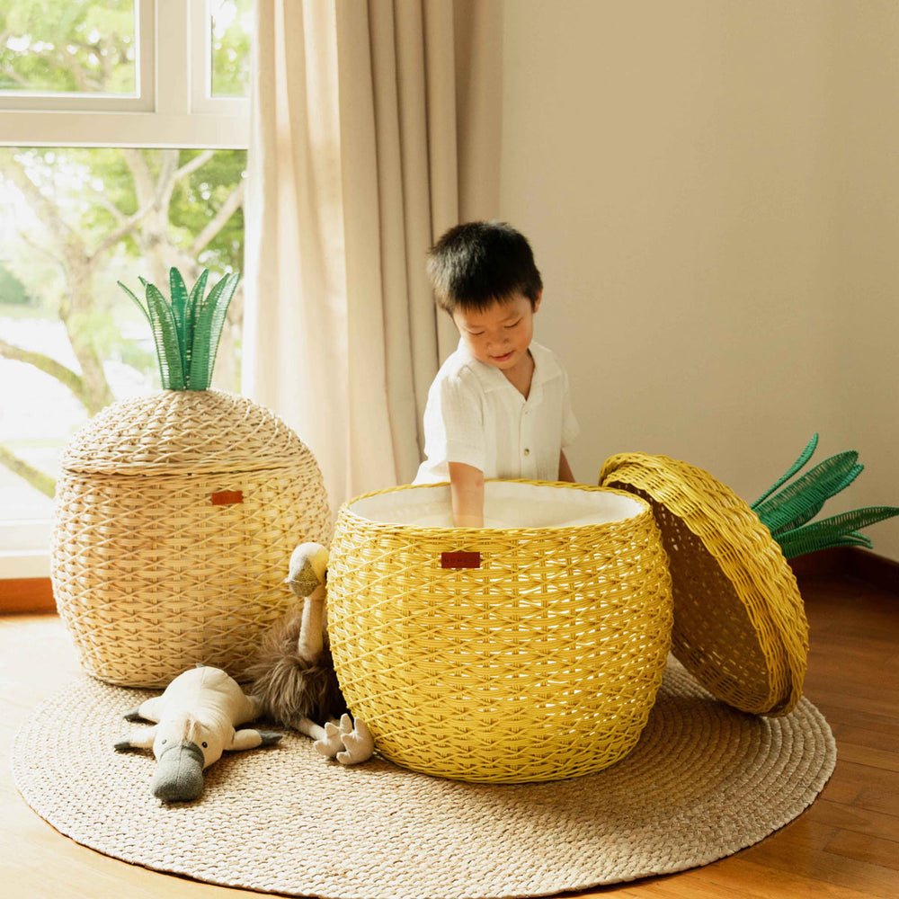 Child playing with the Yellow Pineapple Rattan Storage Basket by MOMIJI, beside the natural colored Pineapple Rattan Storage Basket with stuffed toys on the floor.