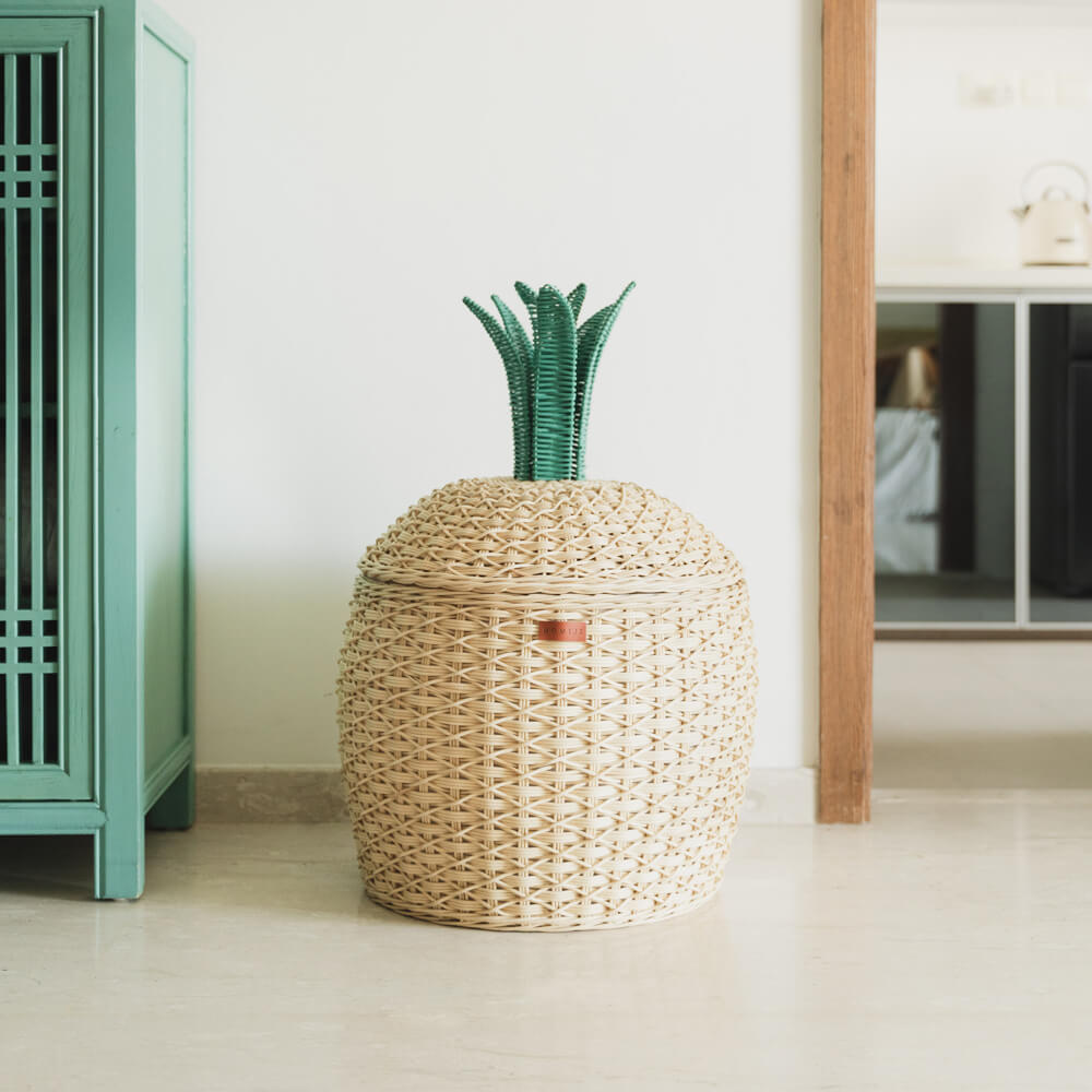 A Pineapple Rattan Storage Basket by MOMIJI  placed on a floor next to a green cabinet.