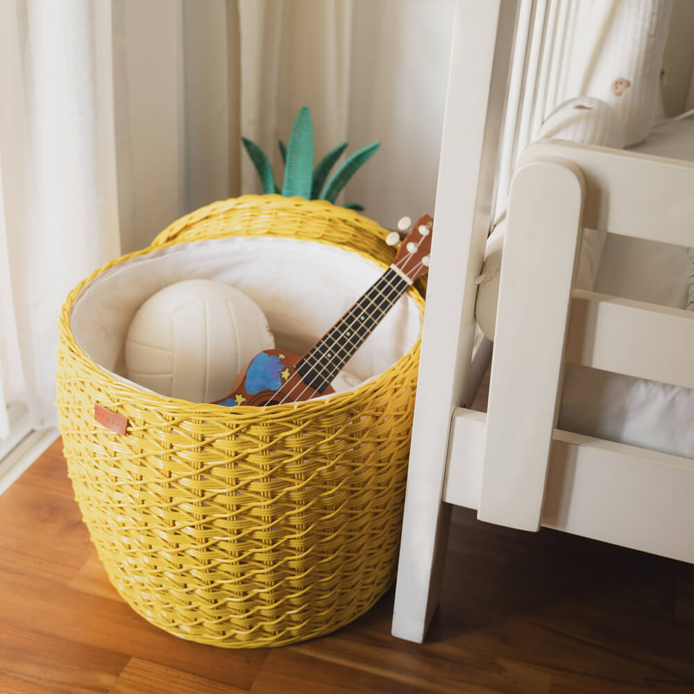 An opened yellow Pineapple Rattan Storage Basket with a ball and a ukulele inside the basket.