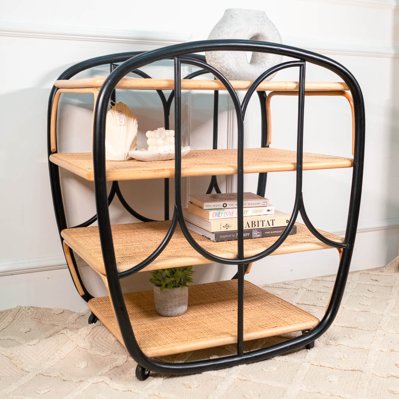 Handcrafted rattan wicker Posy Bar Cart by MOMIJI styled with books and home decor, featuring a black frame, four woven rattan shelves, and smooth-rolling wheels.