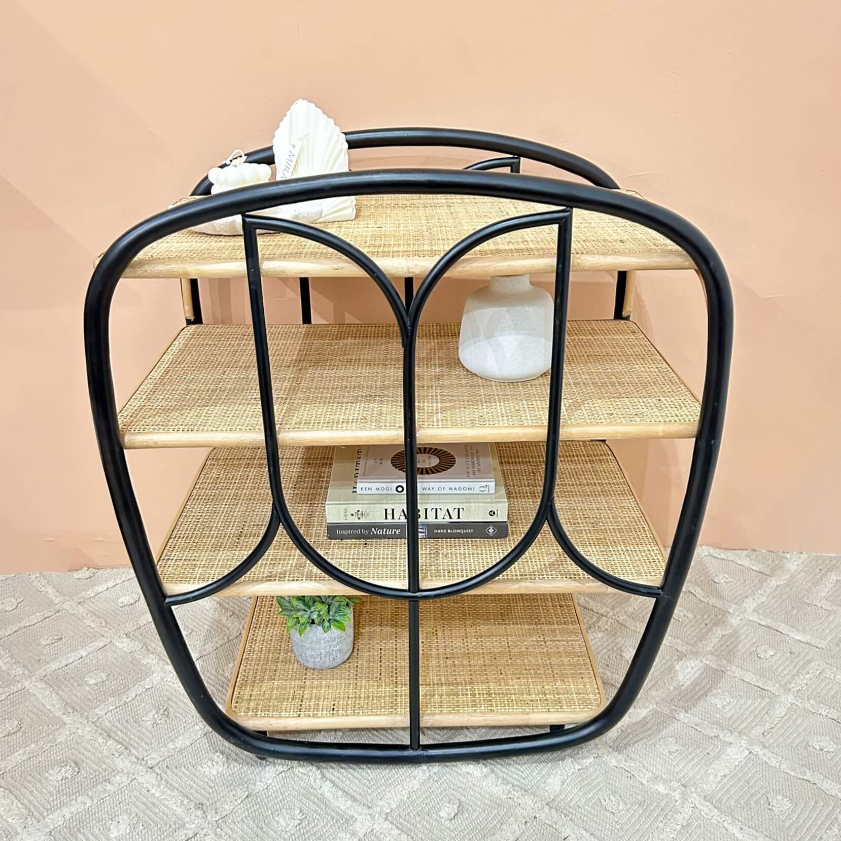 Top view of the handcrafted rattan wicker Posy Bar Cart by MOMIJI showing rattan-woven shelves styled with books and decor, featuring a black frame, four woven rattan shelves on pattern rug.