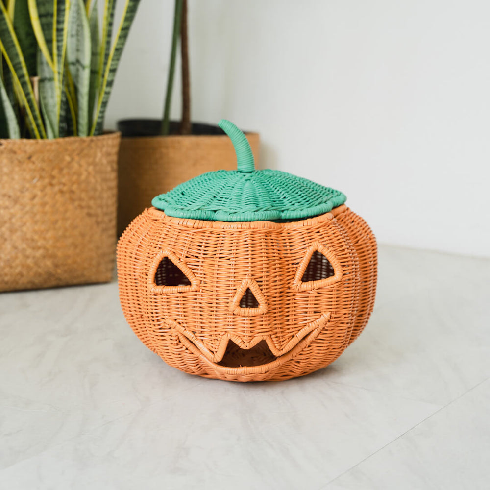 A Pumpkin Face Rattan Basket placed on a tiled surface and plants in the background by MOMIJI. 