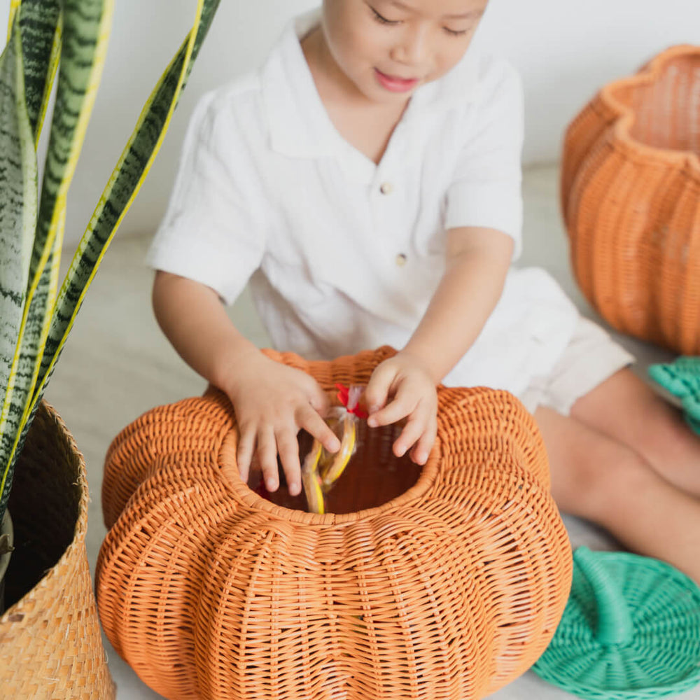 Child putting treats inside the Pumpkin Face Rattan Basket by MOMIJI.