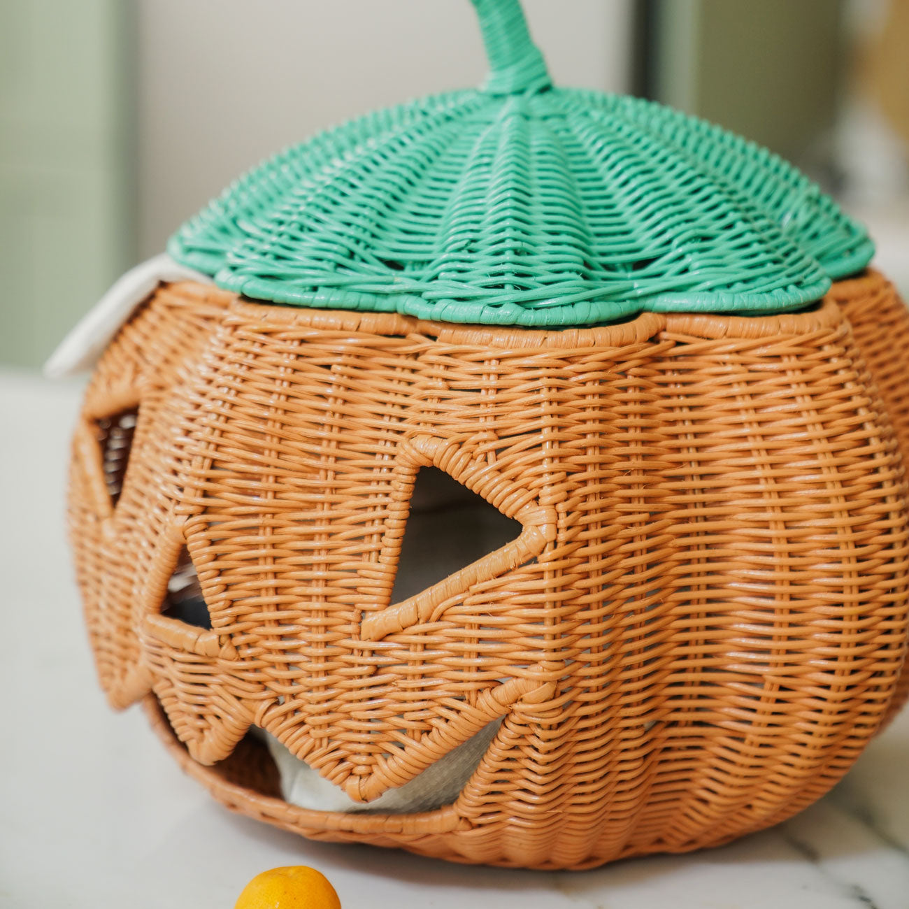 Close-up of the handcrafted Pumpkin Face Rattan Basket by MOMIJI, highlighting its playful jack-o'-lantern face, handwoven rattan details, and mint green lid with a decorative stem.