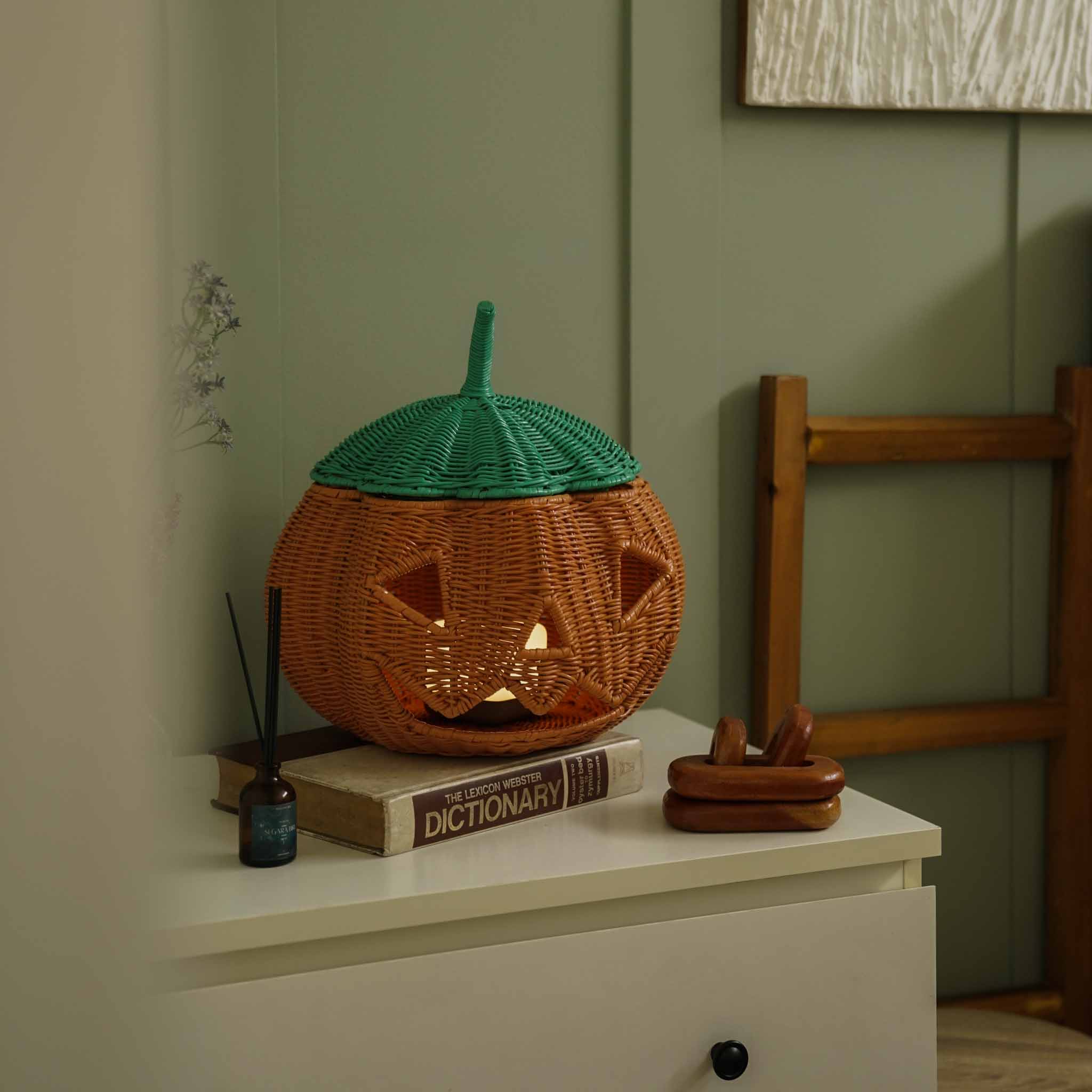 Handcrafted Pumpkin Face Rattan Basket by MOMIJI styled with a soft cube light inside, creating a glowing jack-o'-lantern lantern effect in a cosy room setting.