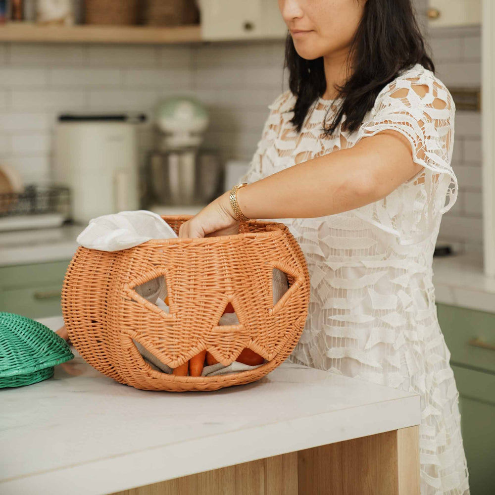 A woman placing a carrots into the handcrafted Pumpkin Face Rattan Basket by MOMIJI, showcasing its multifunctional design for storing toys, textiles, and everyday household essentials.