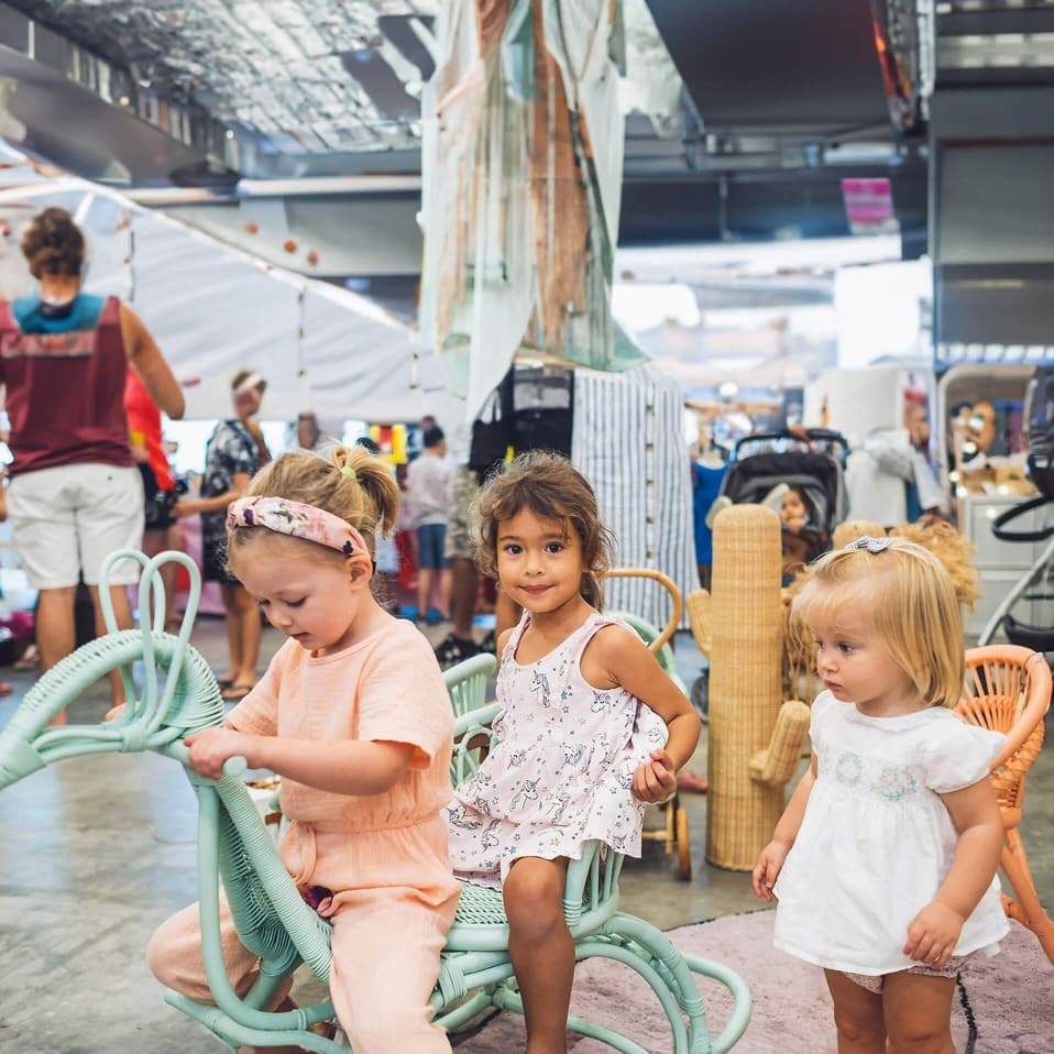 Three young girls enjoying playtime on the Rocking Peacock by MOMIJI in a store setting.