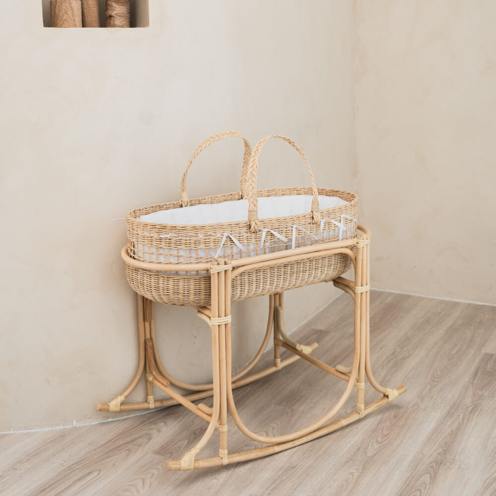 Side view of a wicker Moses basket with rocking stand by MOMIJI in an indoor setting.