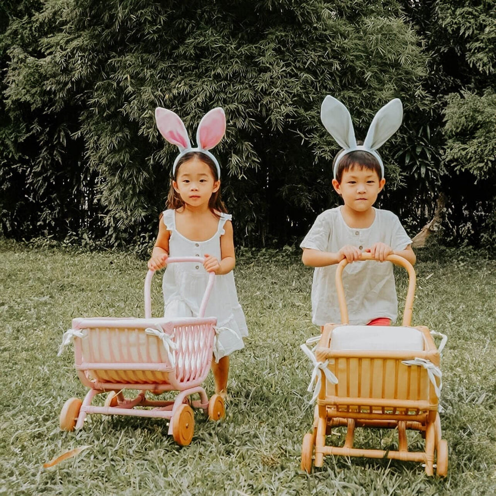 Two children wearing bunny ears playing with natural and pink color of the Rubble Toy Trolleys by MOMIJI outdoors.
