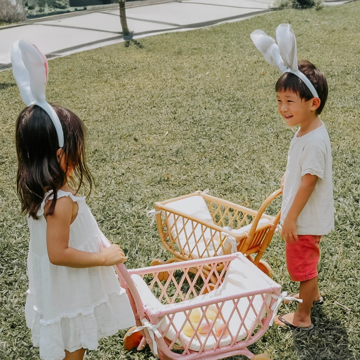 Two children wearing bunny ears enjoying playtime with a pink Rubble Toy Trolley by MOMIJI outdoors.