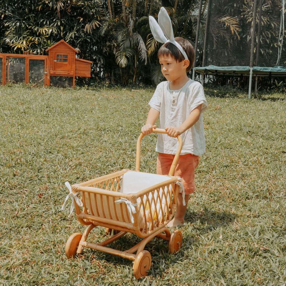 Child pushing the Rubble Toy Trolley by MOMIJI in natural color outdoors while wearing bunny ears.