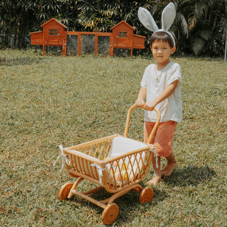 Child wearing bunny ears playing with the natural color of Rubble Toy Trolley by MOMIJI outdoors with wooden houses in the background.