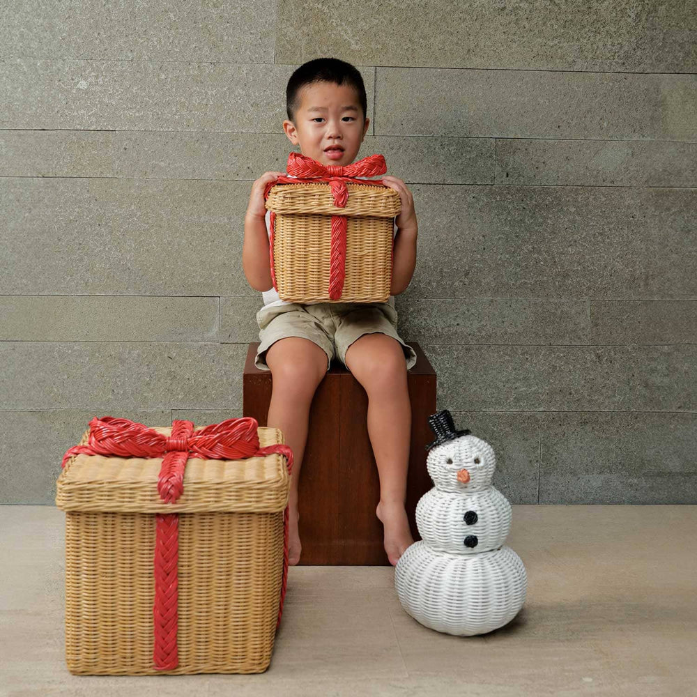 Child holding a small sized rattan basket gift box with snowman rattan basket and large sized rattan basket gift box on the floor.