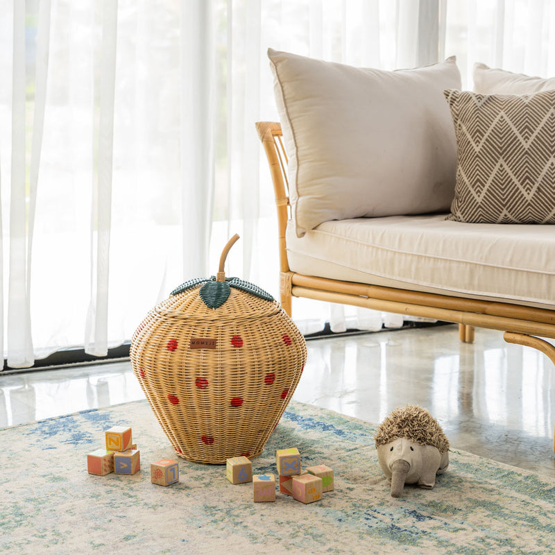 Handcrafted strawberry rattan wicker pineapple storage basket by MOMIJI, featuring a green leaf and natural stem lid, styled in a living room with children’s toys and a rattan bench.